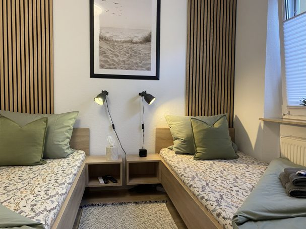 Schlafzimmer mit 2 Einzelbetten Helles Schlafzimmer mit zwei Betten, grünen Kissen und einem Bild an der Wand.