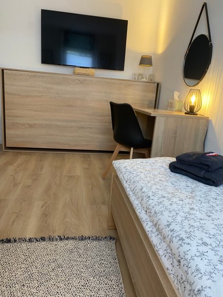 Schlafzimmer mit 3 Einzelbetten Helles Zimmer mit Holzmöbeln, Fernseher und Schreibtisch.